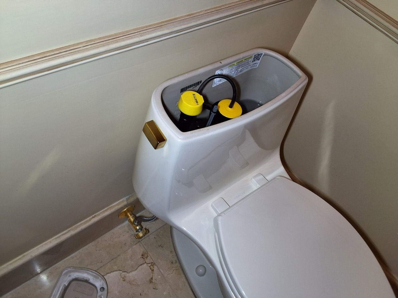 Toilet tank filled with water, with a yellow and black cleaning or repair device inside