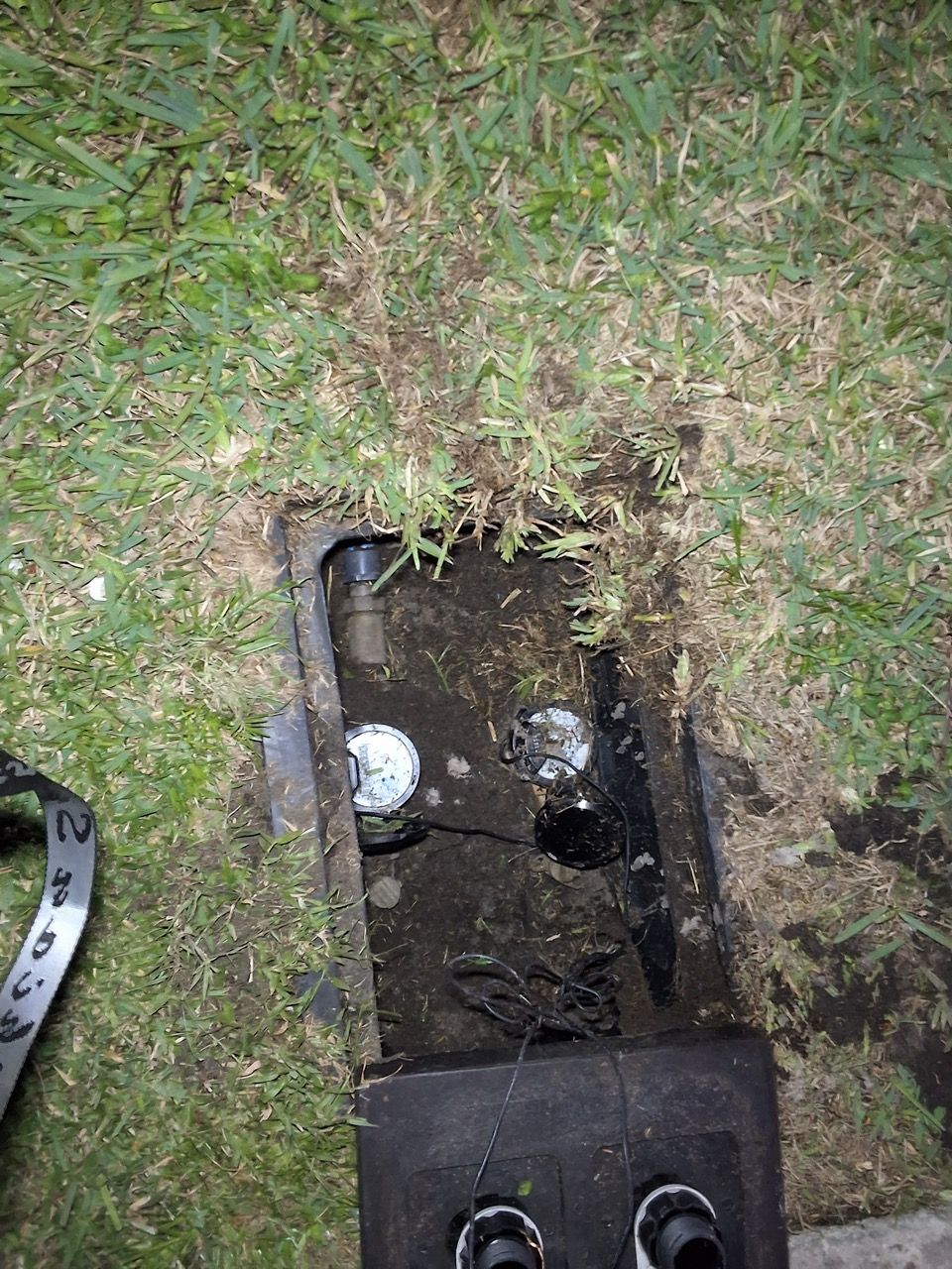 Open utility box in grass with exposed pipes and muddy interior