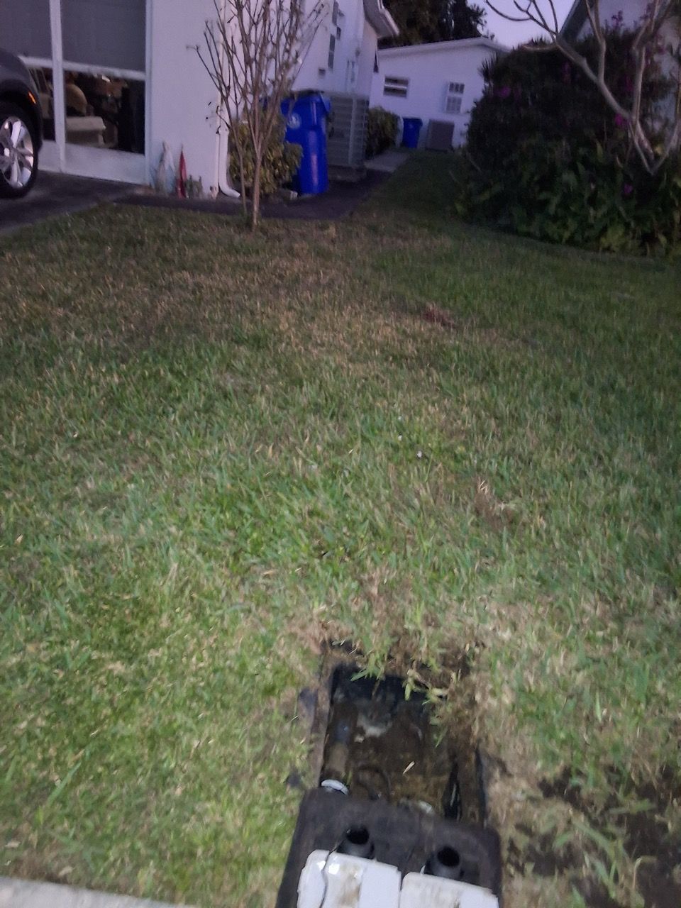 Nighttime front yard with a grass lawn, a hole in the ground, and a house in the background