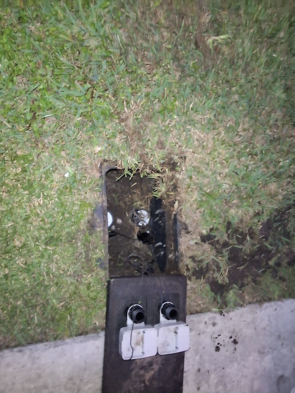 Open utility box in grass beside concrete, with exposed pipes and two white meter caps