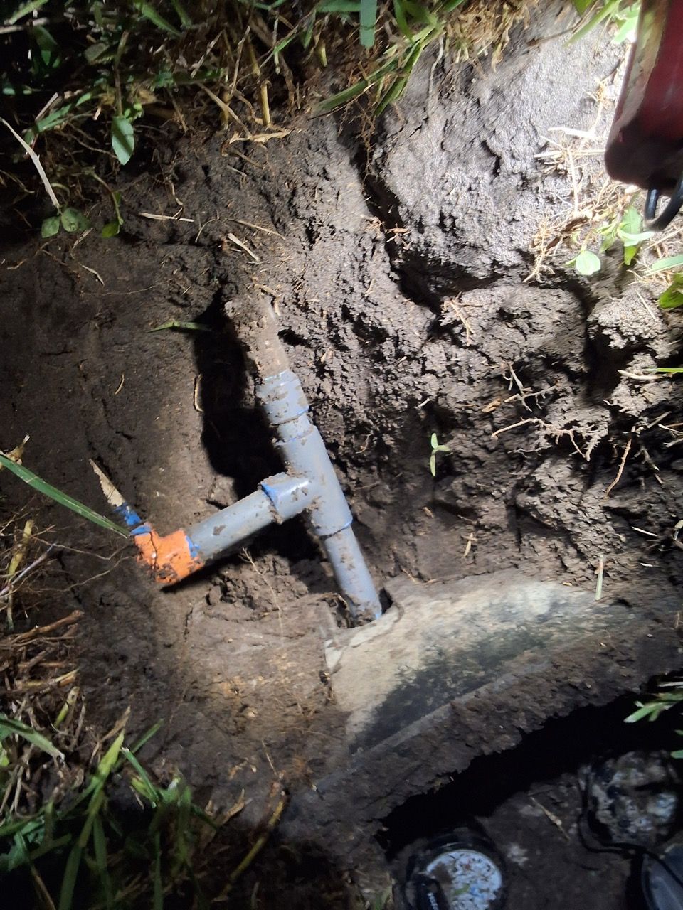 Broken gray pipe in muddy excavation trench, with water pooling at the bottom.