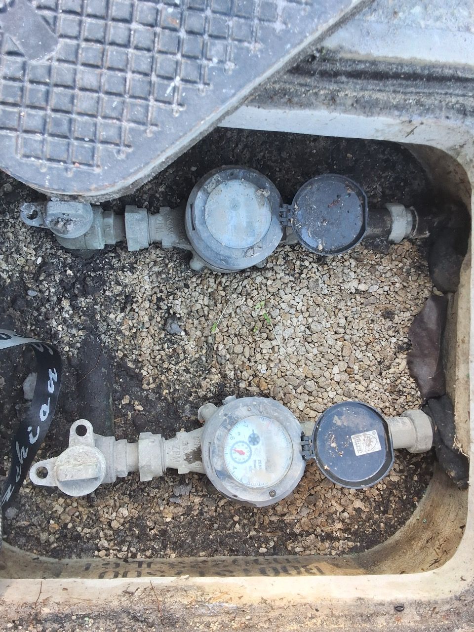 Gas meter and valves in a dirty utility pit with gravel and debris.