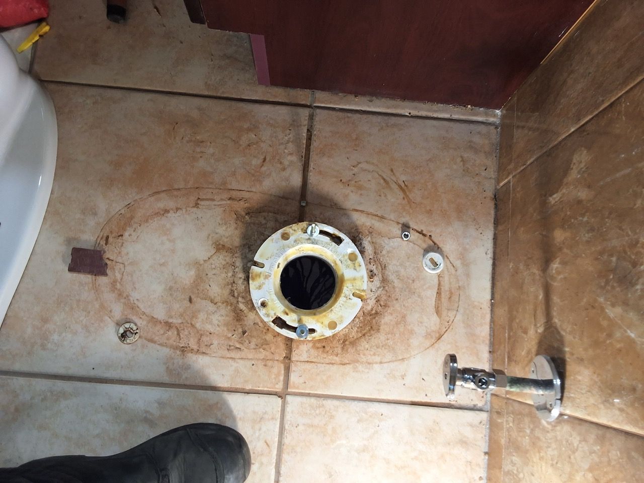 Rusty floor drain inside a brown-tiled shower stall, with a faucet handle on the right.