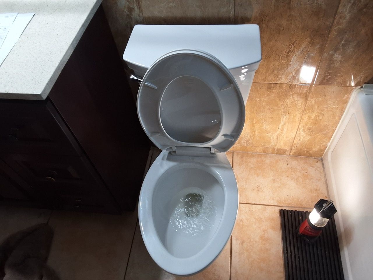 Open toilet in a bathroom with a dark vanity and tiled floor, viewed from above.