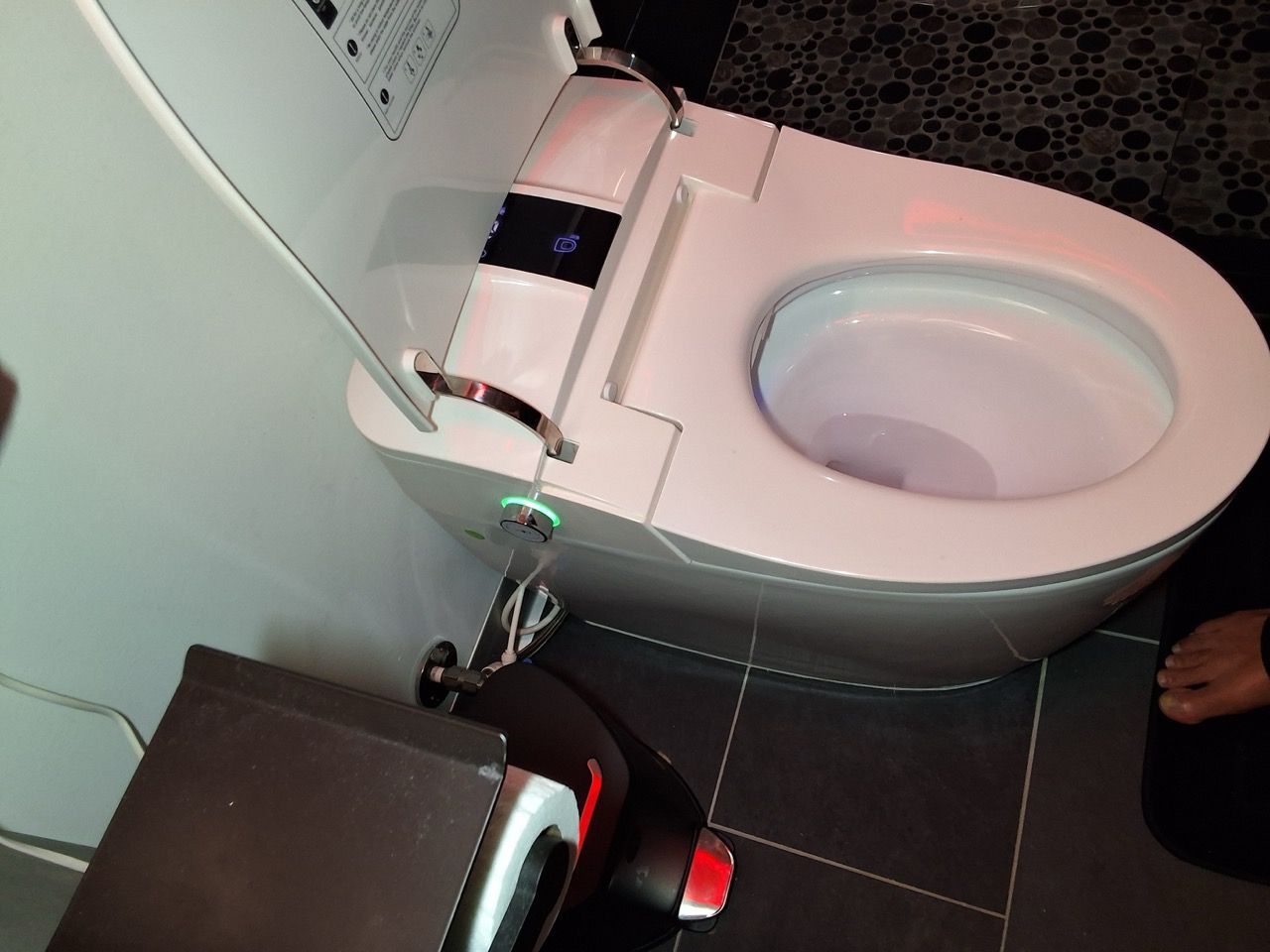 Open toilet next to a dark trash bin in a tiled bathroom stall