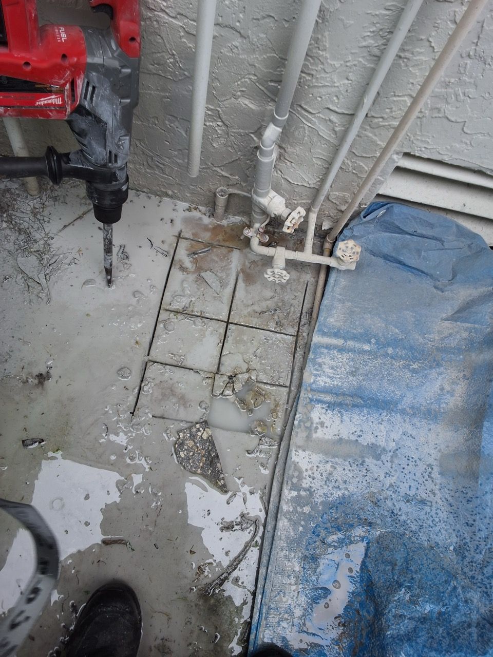 Construction drill near wet concrete floor with pipes and a blue tarp on the right