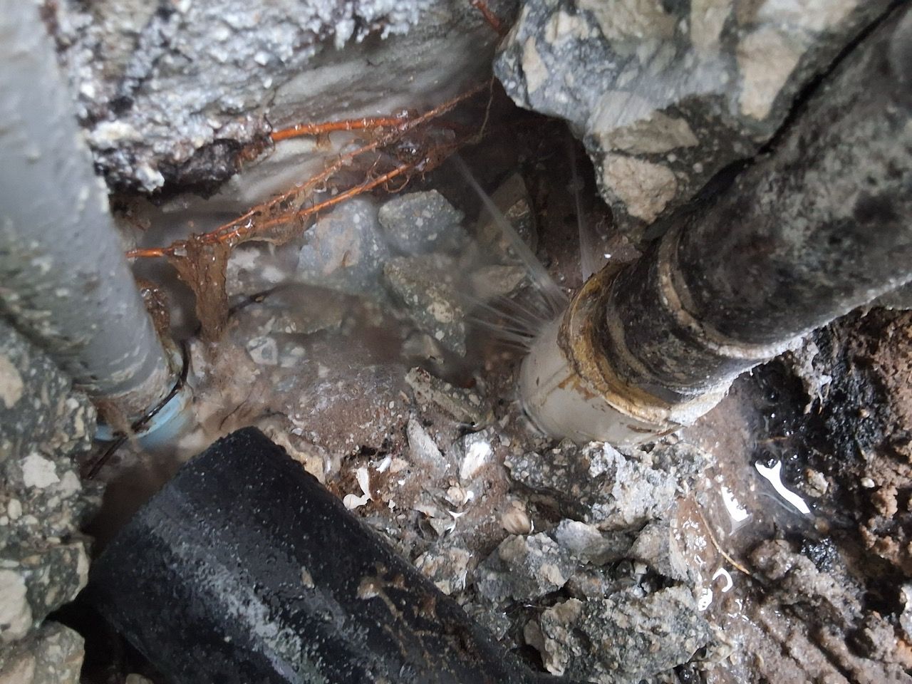 Damaged basement floor with exposed pipes, wet debris, and cracked concrete around a drain area