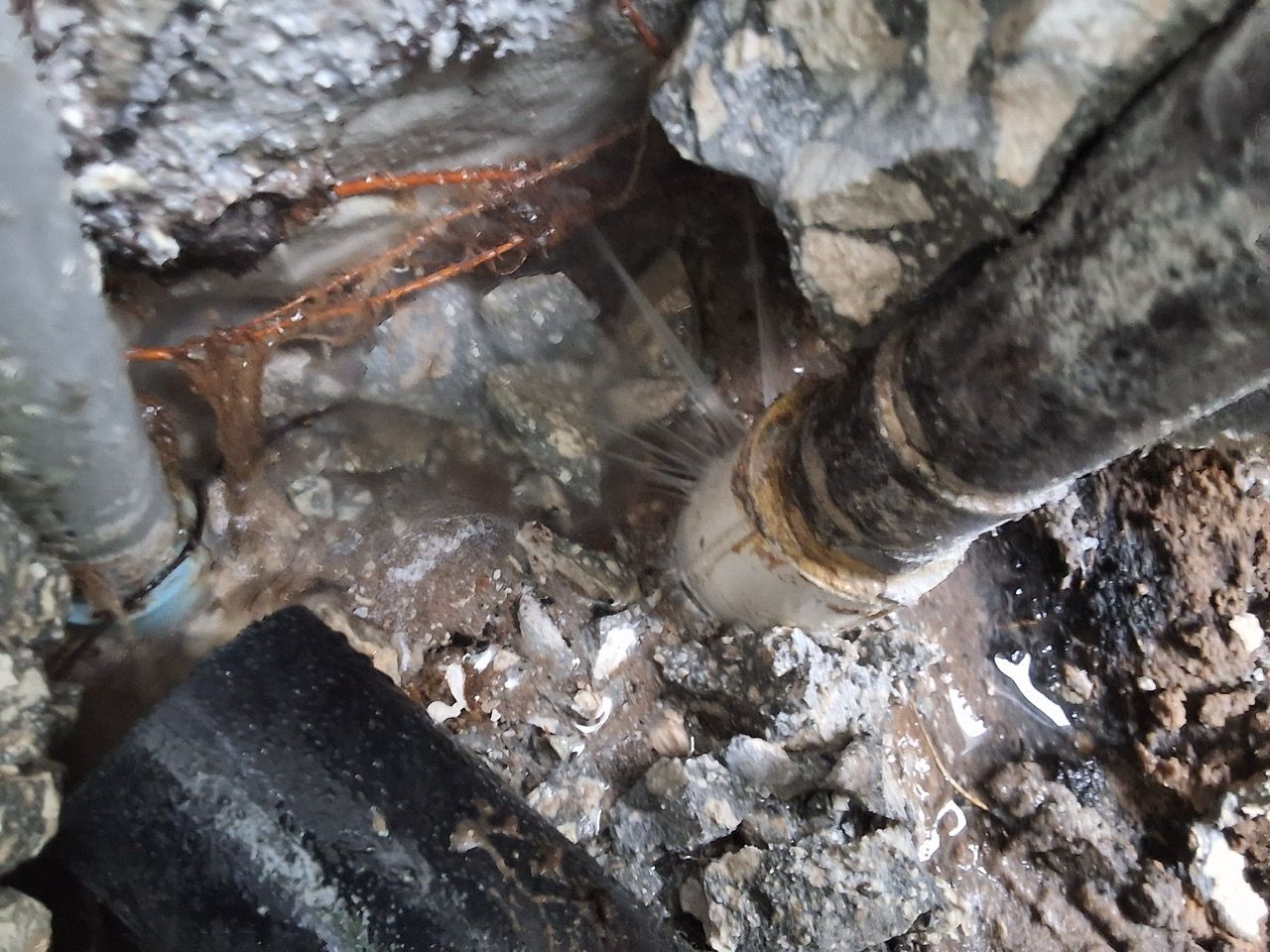 Damaged pipes and rubble in a wet crawl space with a black insulated hose