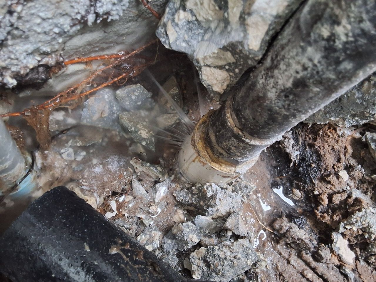 Close-up of a rusted metal pipe leaking water onto rocks and debris in a wet crevice