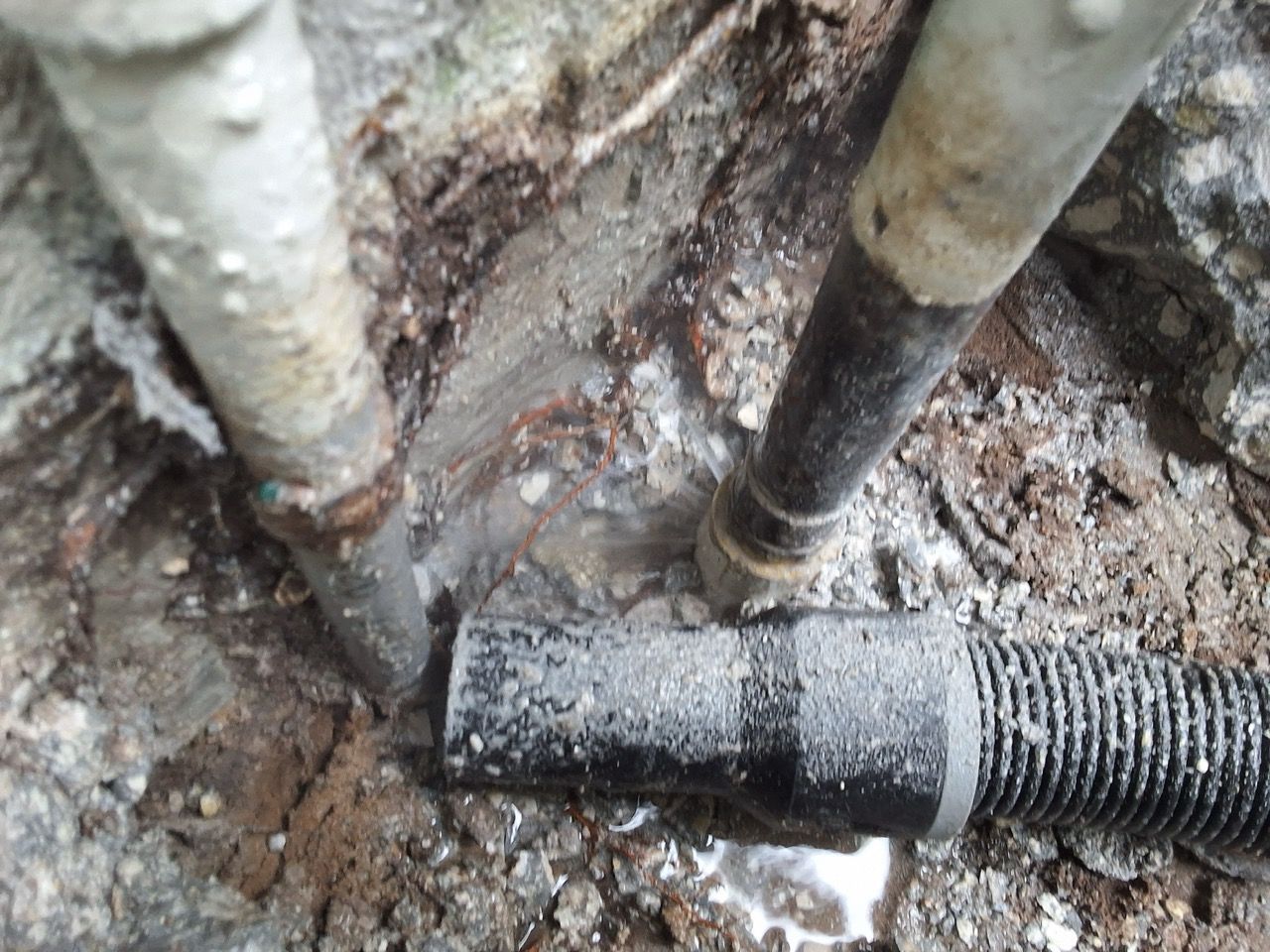 Close-up of muddy ground with two pipes and a black corrugated hose connection