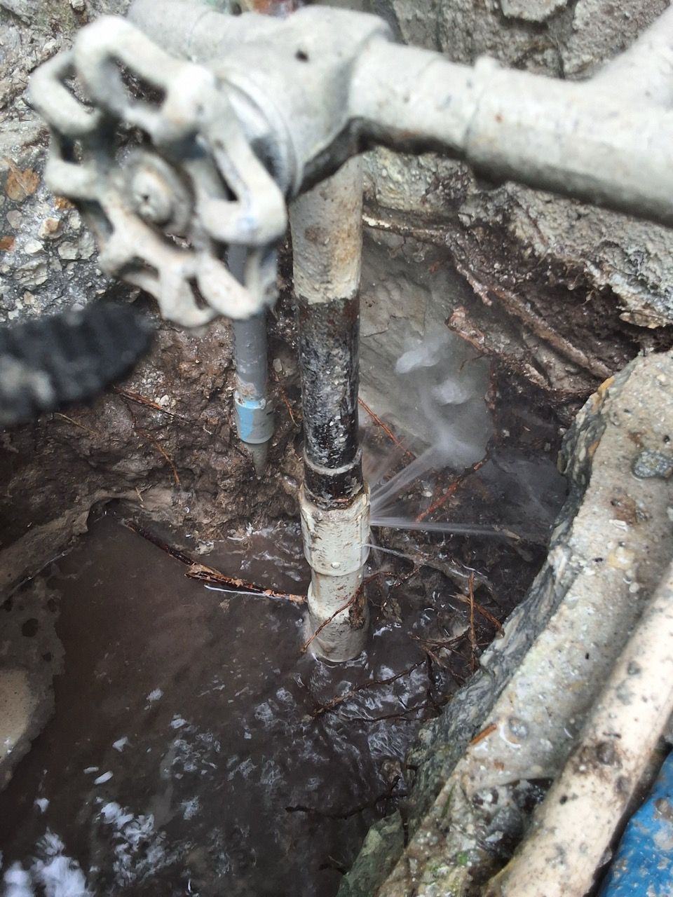 Leaking outdoor pipe valve over muddy ground with flowing water