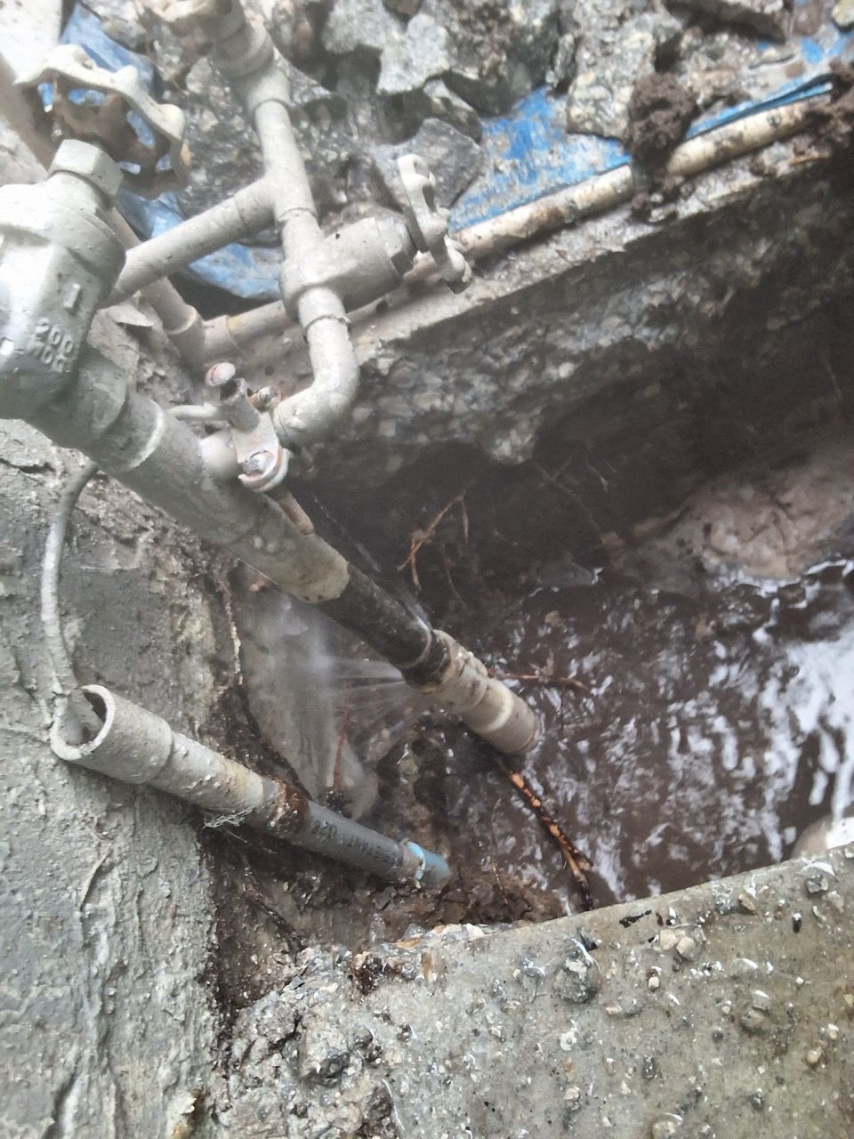 Excavation pit with several gray pipes and muddy water in a concrete trench