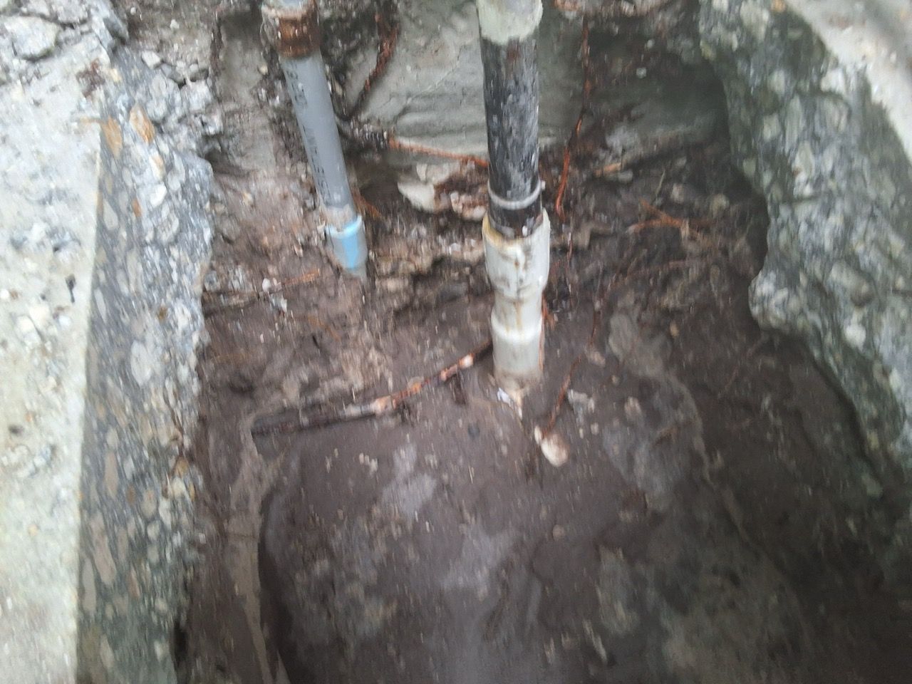 Open pit with exposed pipes and muddy soil inside a rough concrete excavation