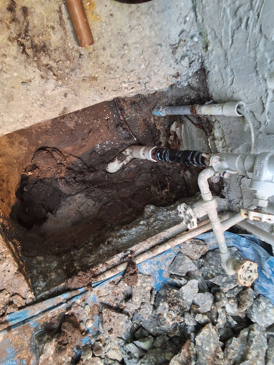 Damaged wall with exposed pipes, a dark hole, and rubble on the floor