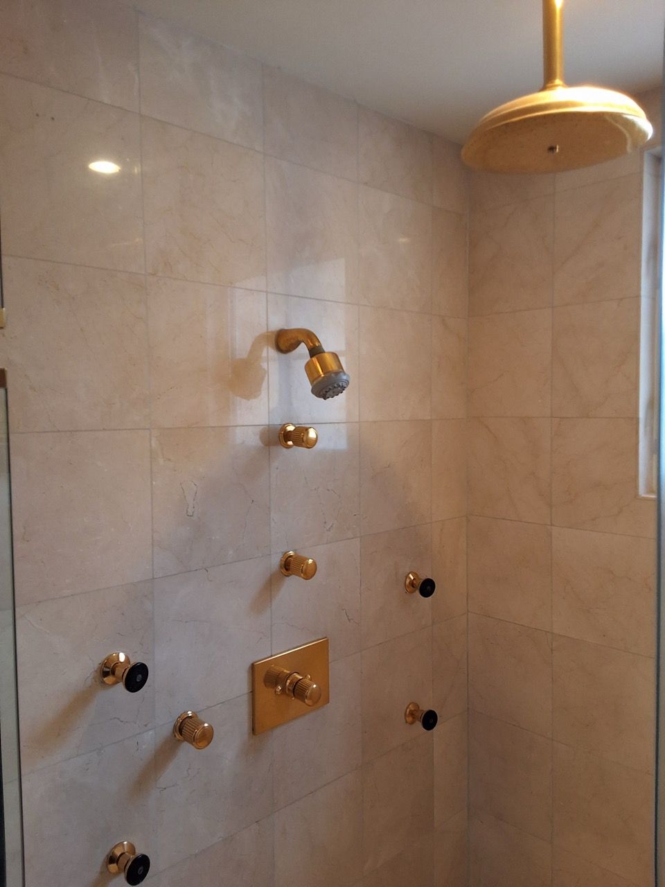 Shower stall with beige tile, brass fixtures, and a wall-mounted showerhead.