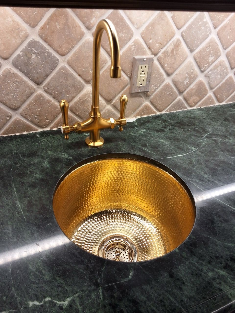 Gold faucet and sink in dark marble countertop with tiled backsplash