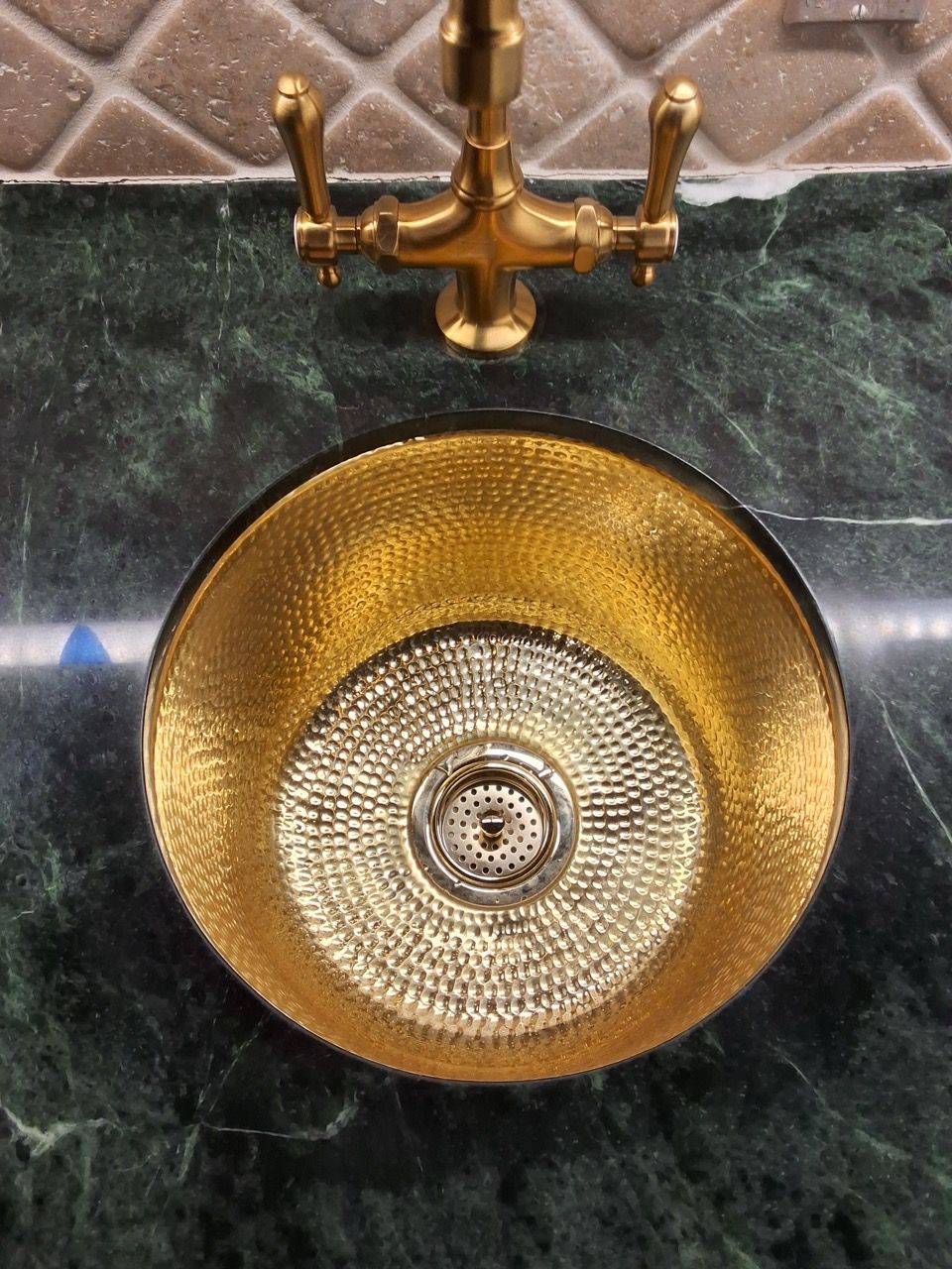 Brass faucet above a gold sink basin on dark green marble countertop, viewed from above