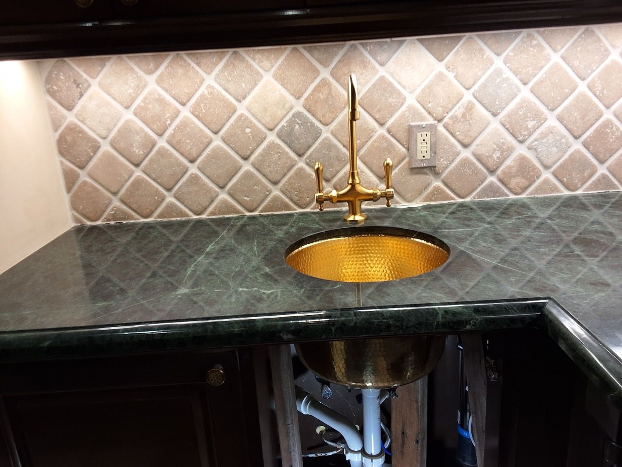 Kitchen sink with green countertop, gold faucet, and tiled backsplash.
