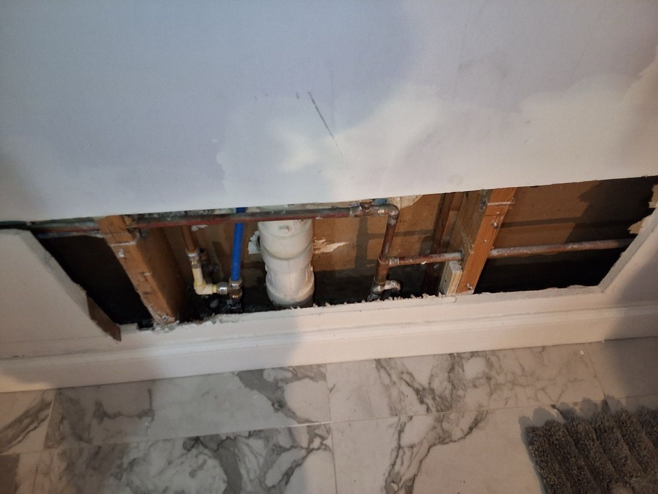 Damaged bathroom ceiling with exposed pipes and drywall above tiled wall and floor