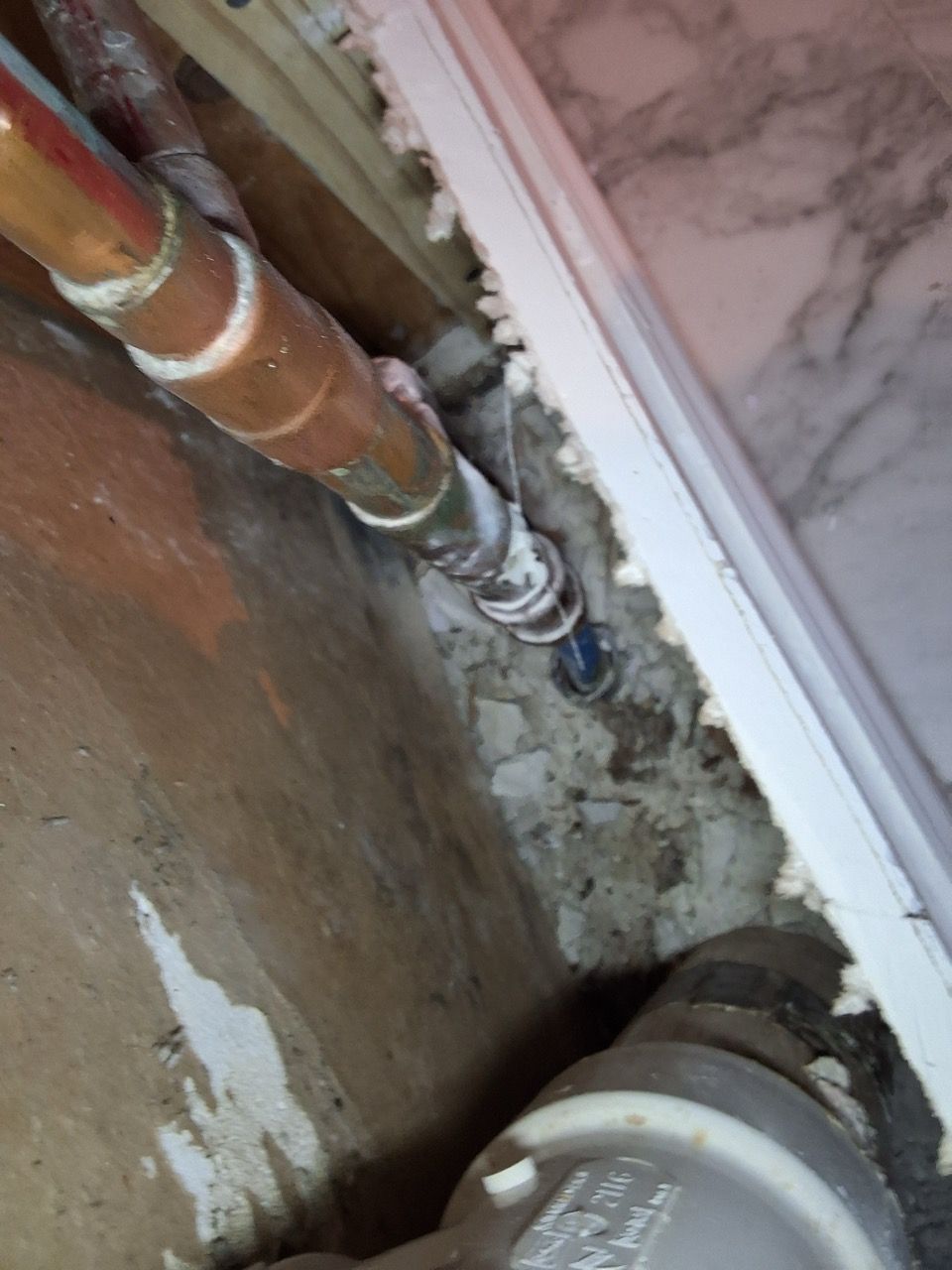 Copper pipes and a wall opening with exposed rough plaster near a tiled floor.