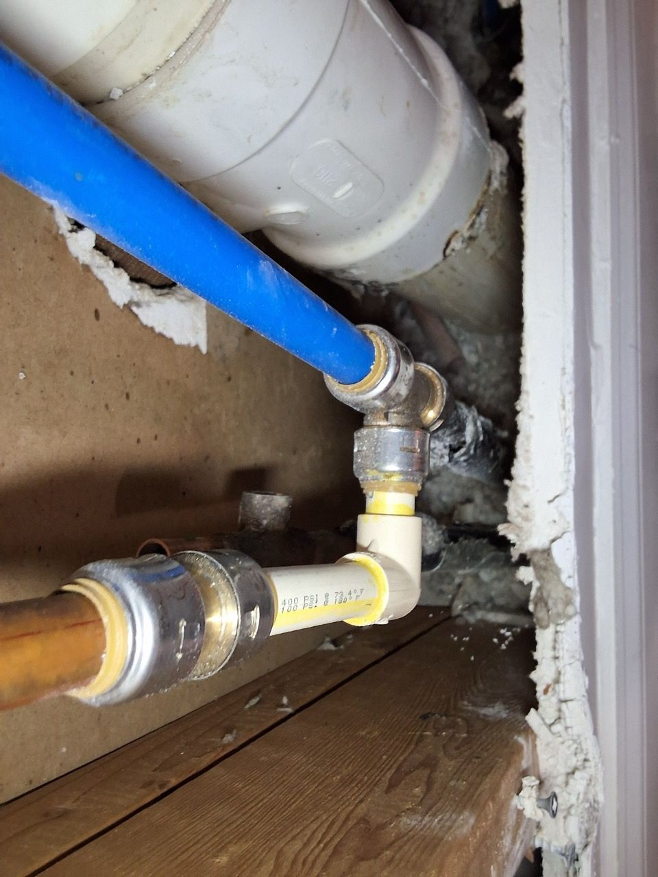 Blue and white plumbing pipes connected with fittings in a narrow wall cavity