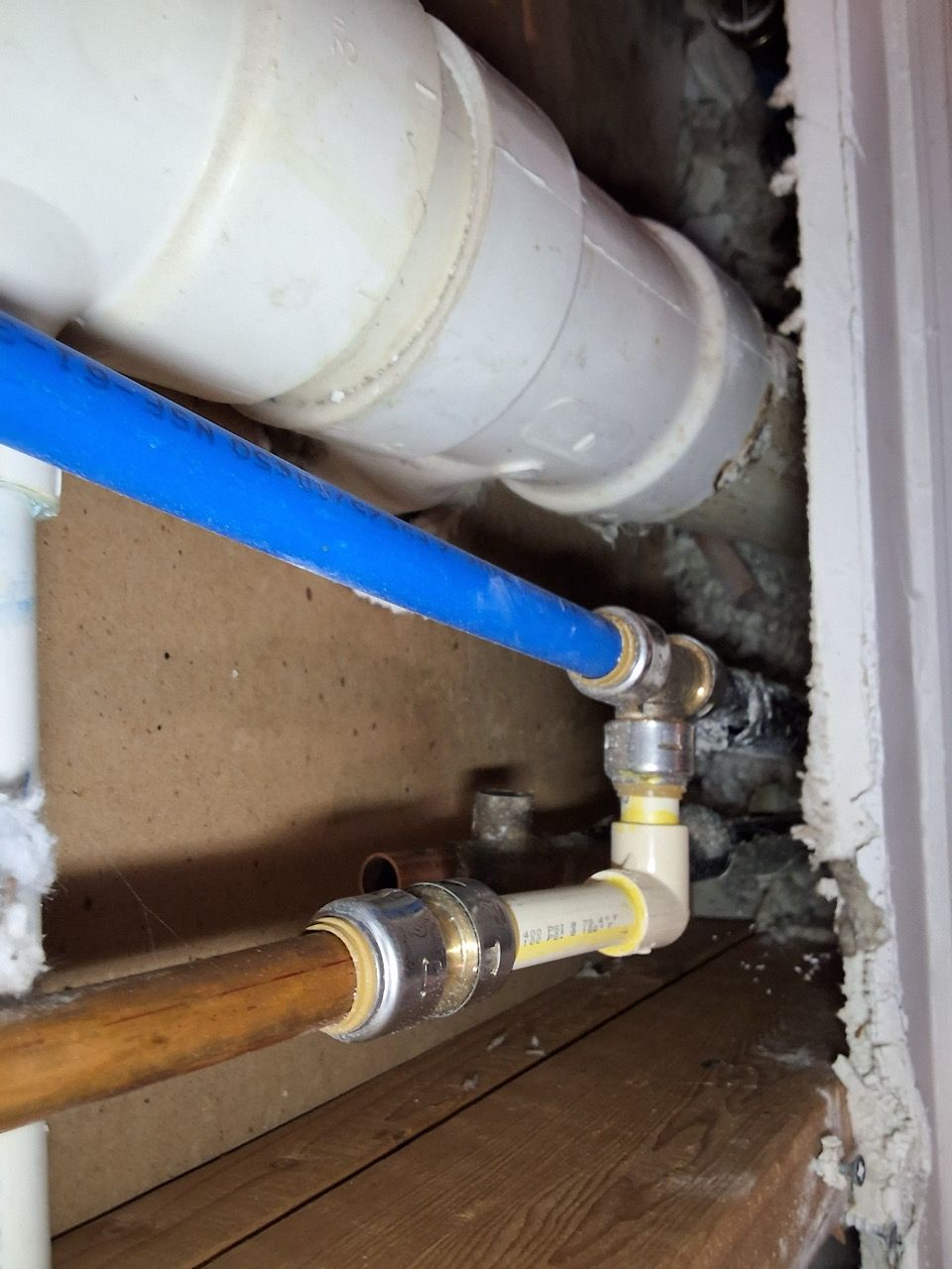 Close-up of plumbing pipes and fittings under a floor, including a blue pipe connected to white and copper lines