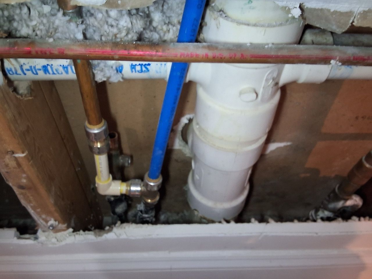 Exposed plumbing pipes and valves inside a wall with a white drainpipe and blue PVC pipe