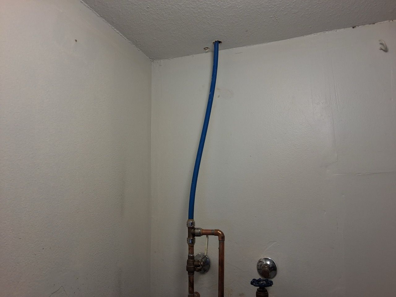 Blue pipe and plumbing fixtures in a white corner wall near the ceiling