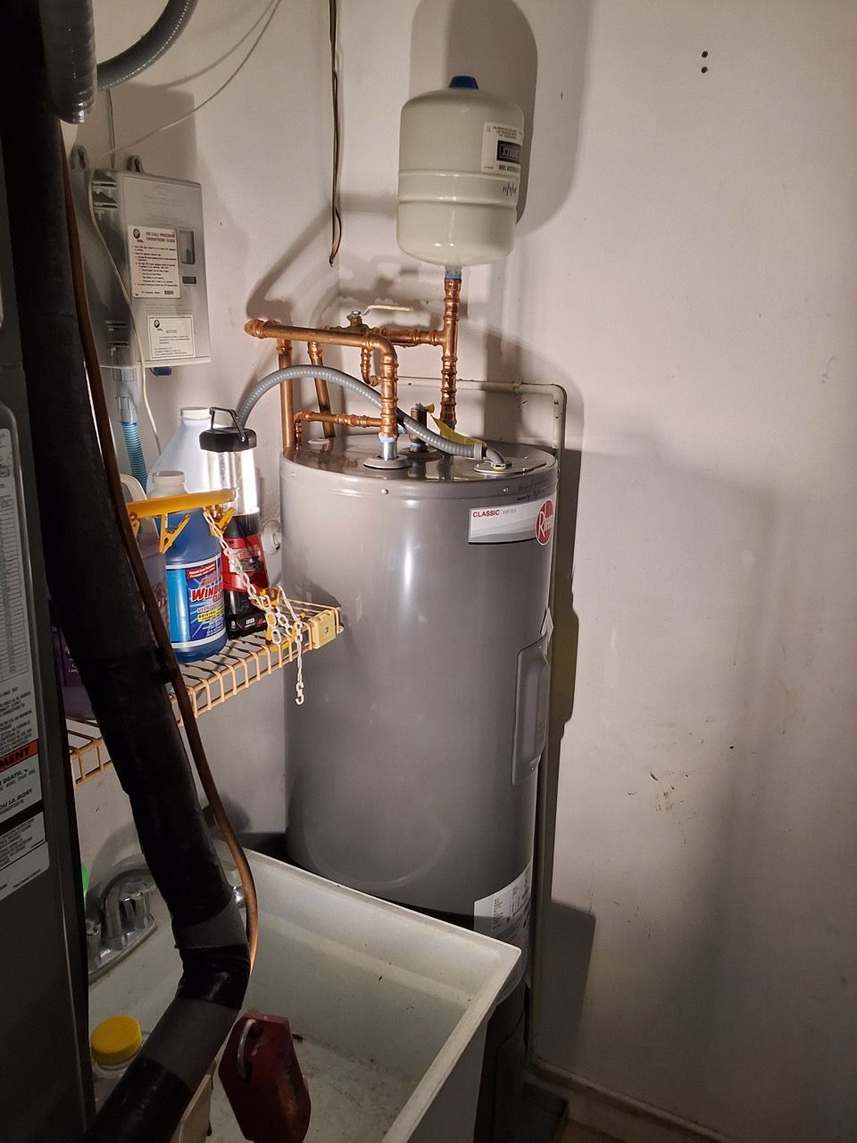 Utility room with a large gray water heater, copper pipes, and laundry items on shelves.