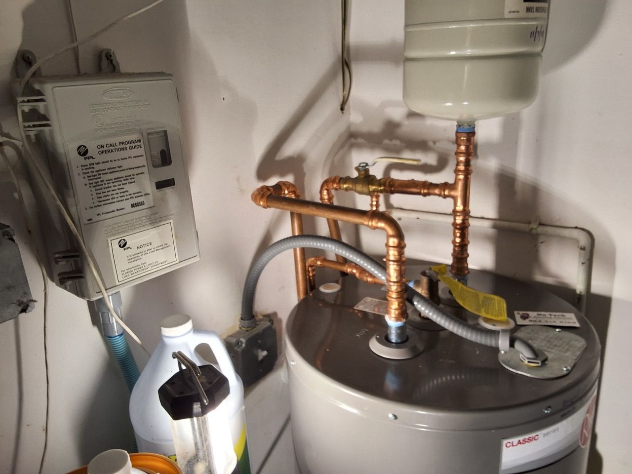 Hot water heater with copper pipes and a nearby control box in a utility closet