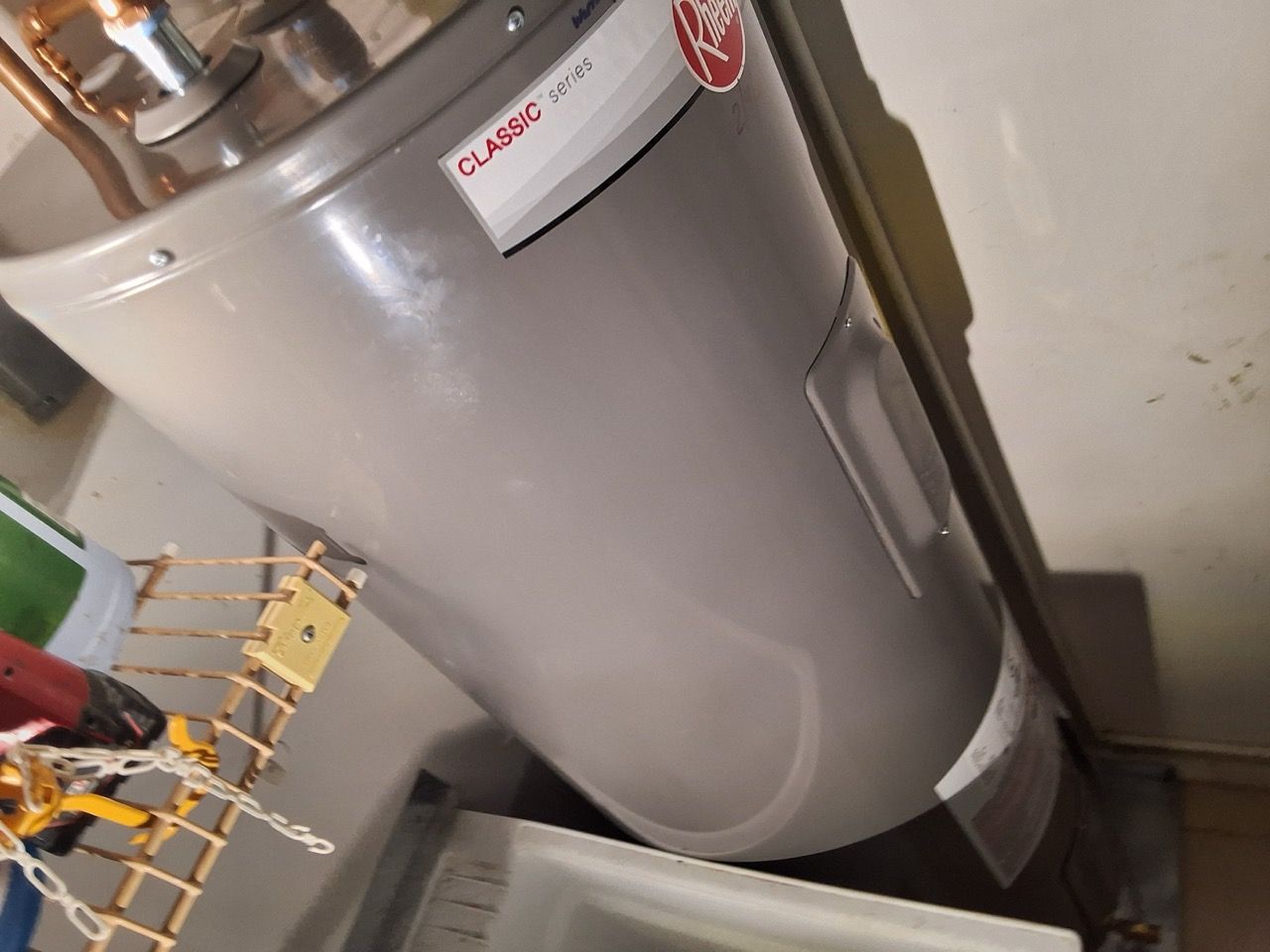 White water heater in a utility room beside pipes and wiring.
