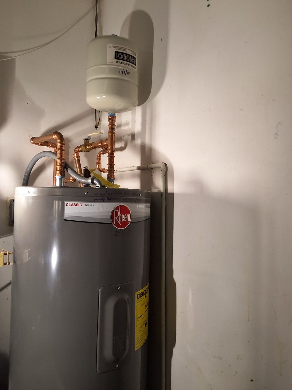 Water heater with copper piping and a white expansion tank in a utility closet