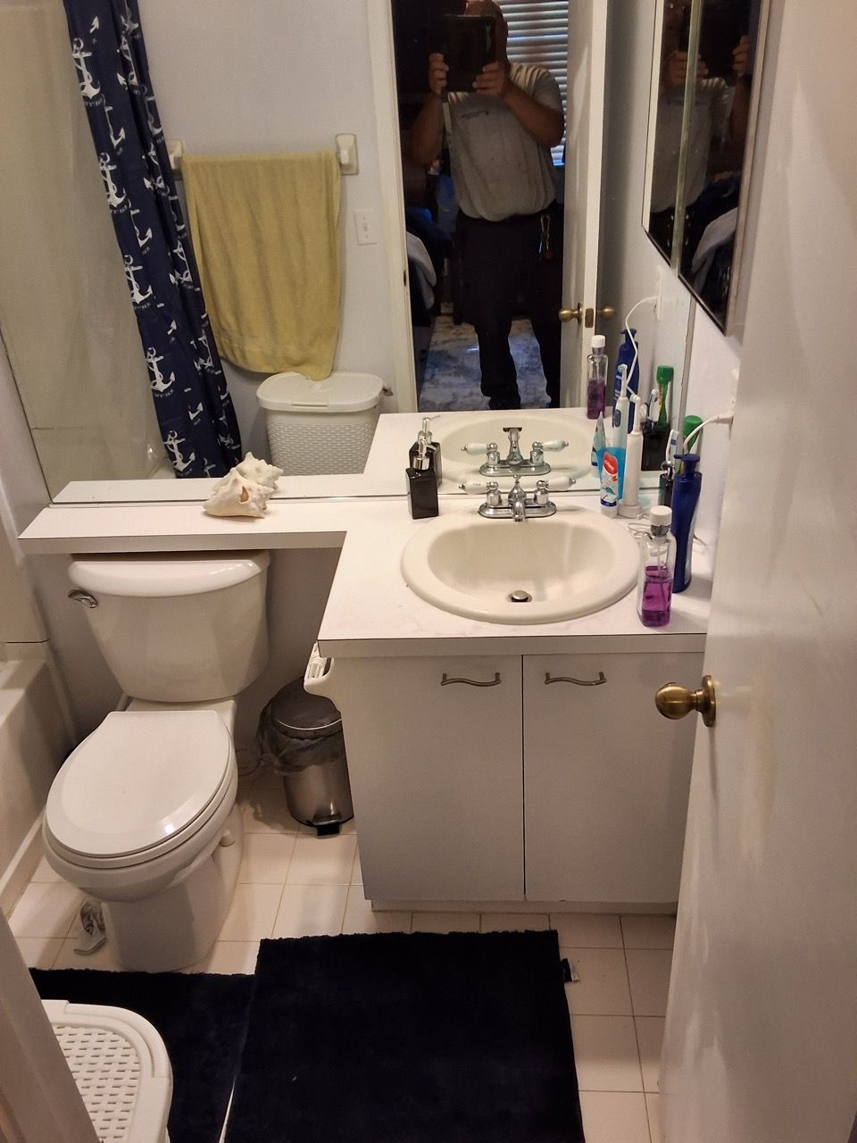 Small bathroom with toilet, sink, mirror, bathtub, and dark rug; a person is reflected in the mirror.