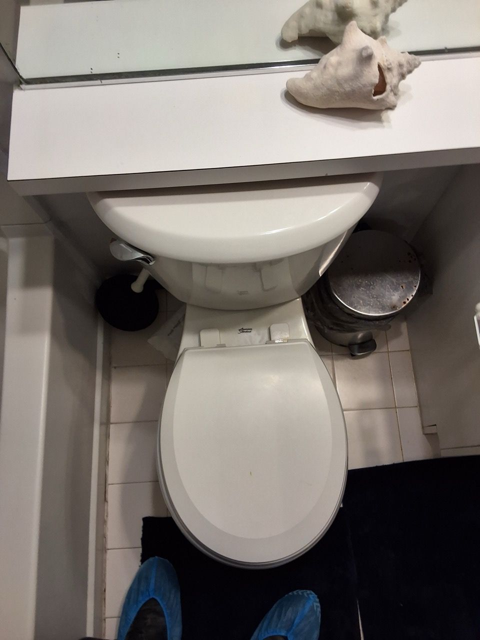 Small bathroom with a toilet, sink, trash can, and a cloth on the counter.