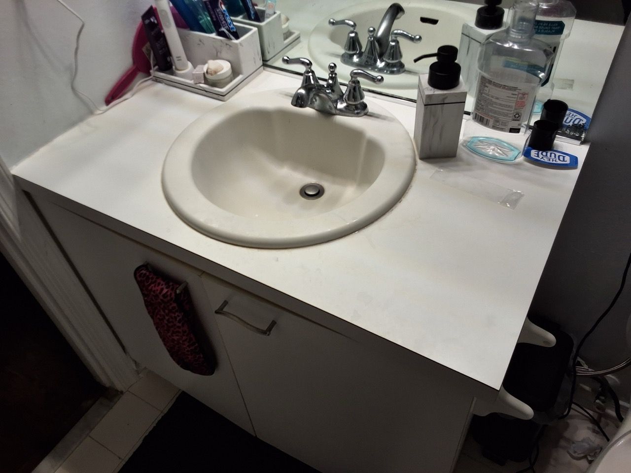 Bathroom sink and vanity with mirror, faucet, toiletries, and a white countertop.