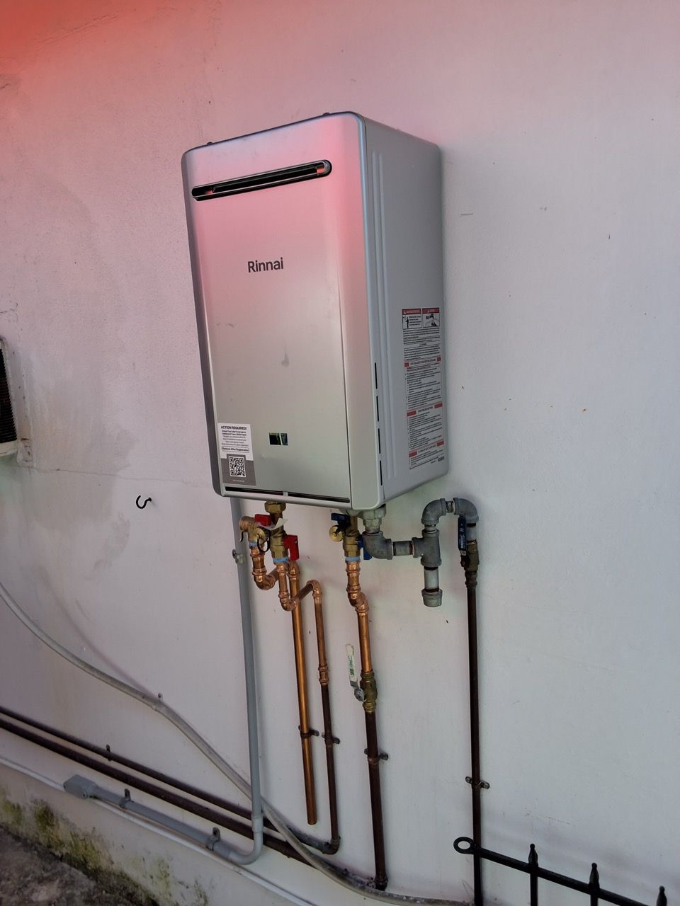 Wall-mounted white water heater with exposed copper pipes in a utility room