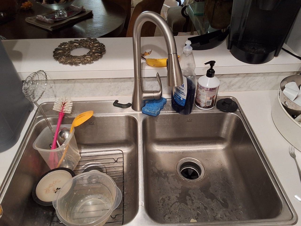 Kitchen sink with dishes, cups, and cleaning tools beside a faucet and soap dispenser