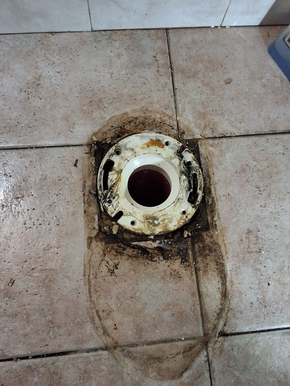 Dirty floor drain opening in beige tiled floor with rust and grime around the rim