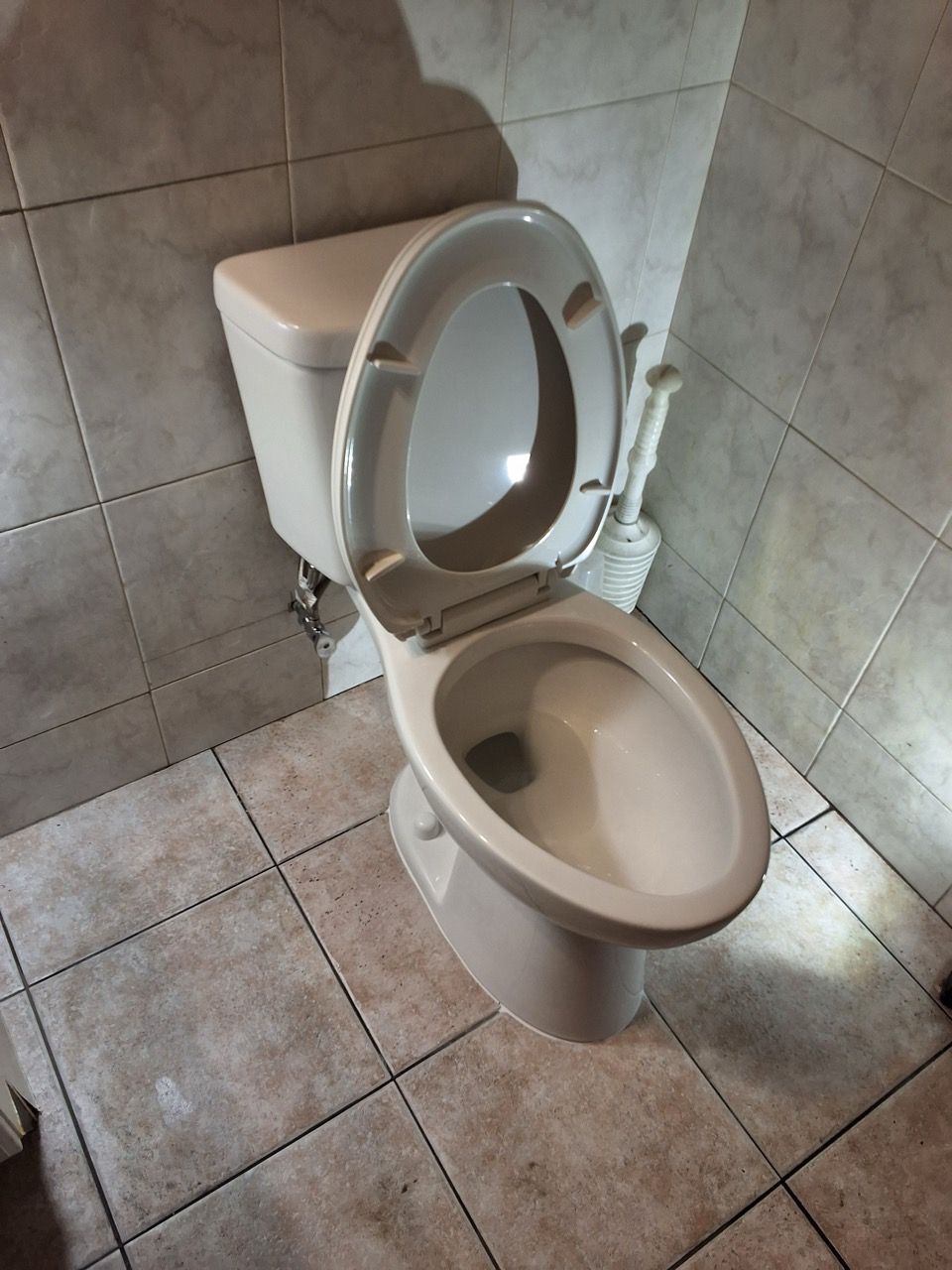 Open toilet with raised seat in a small tiled bathroom corner.