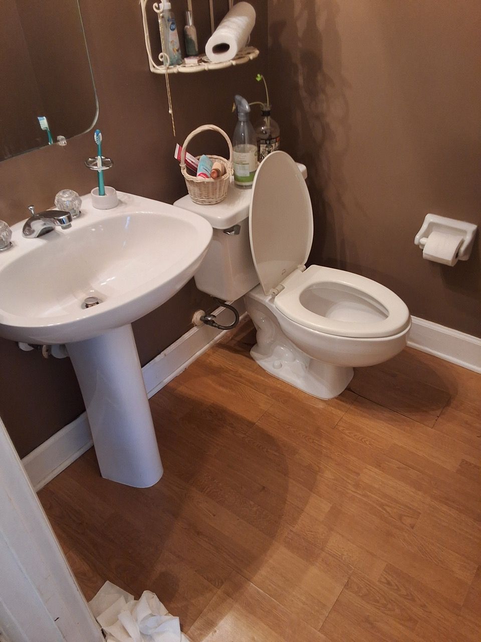 Small bathroom with pedestal sink, toilet, brown walls, and wood floor.