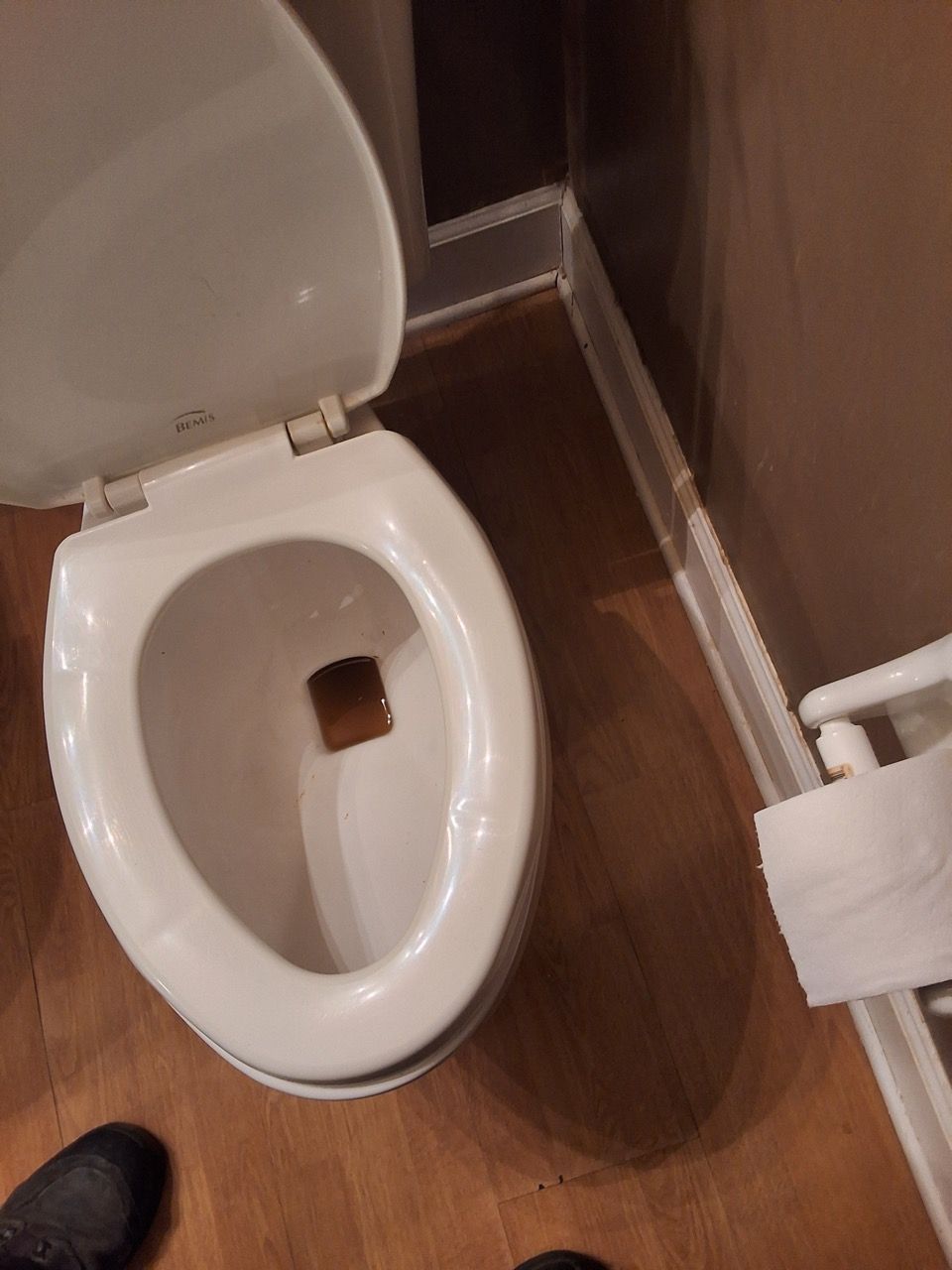 Open toilet bowl in a restroom with a toilet brush holder on the floor beside it.