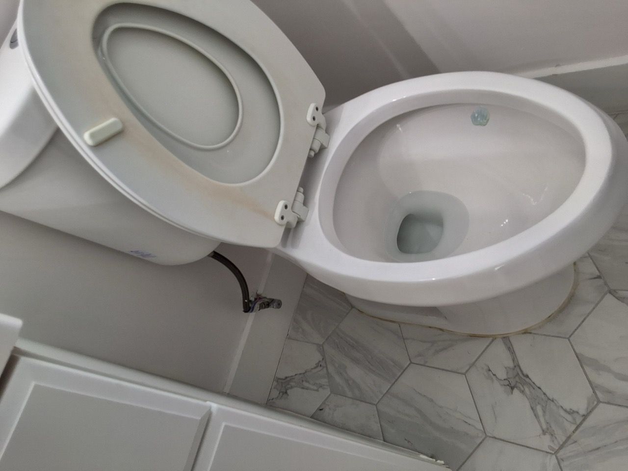 Open toilet seat and bowl in a small tiled bathroom.