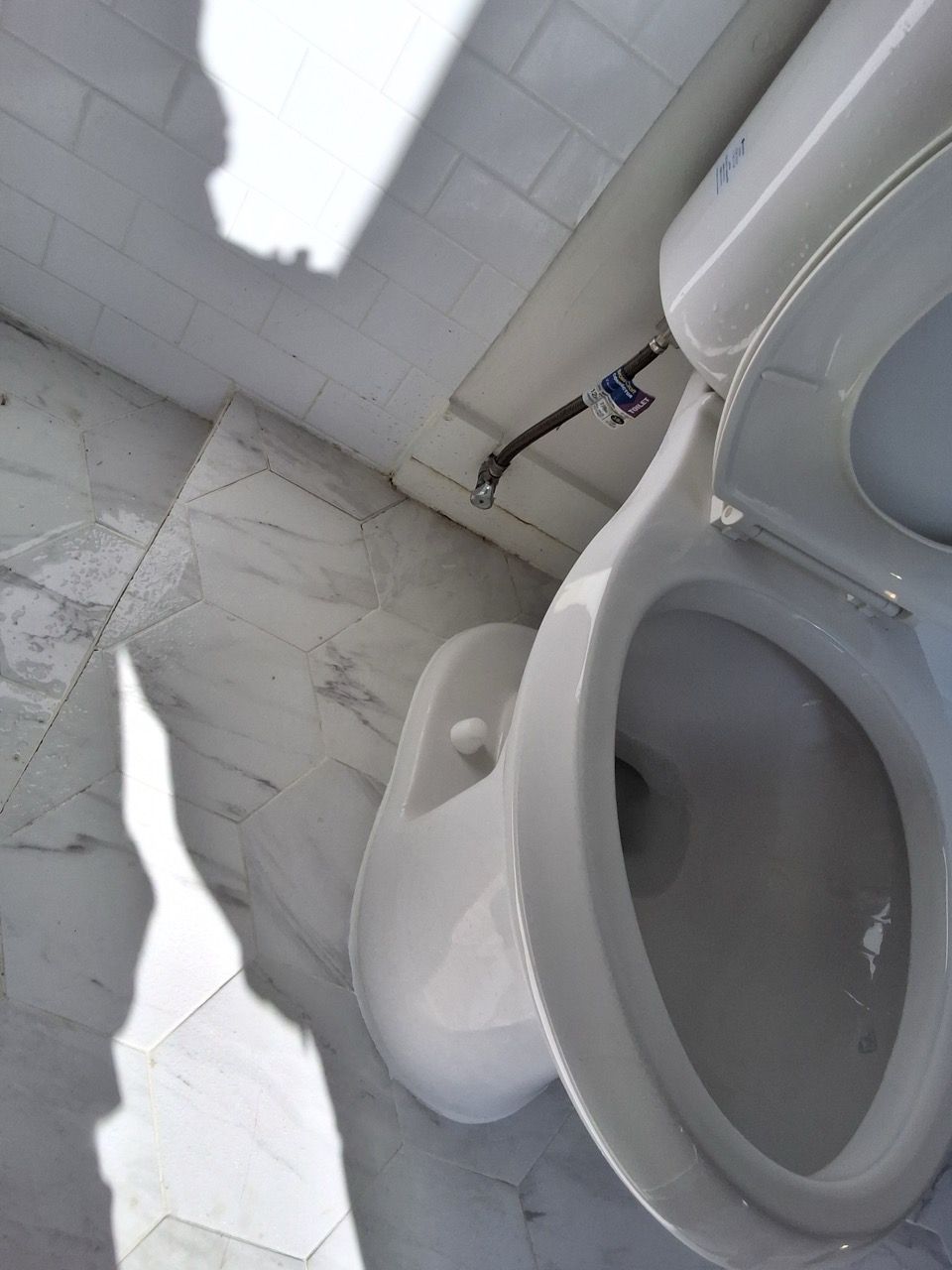 Tilted bathroom with a white toilet and sink against a tiled wall.