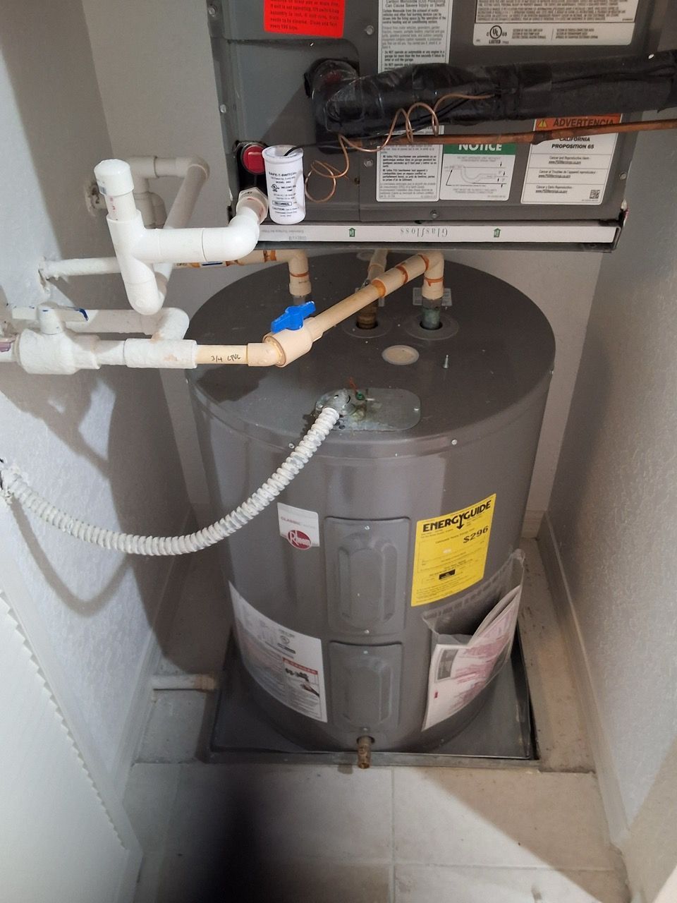 Gray water heater with white pipes and valves in a utility closet
