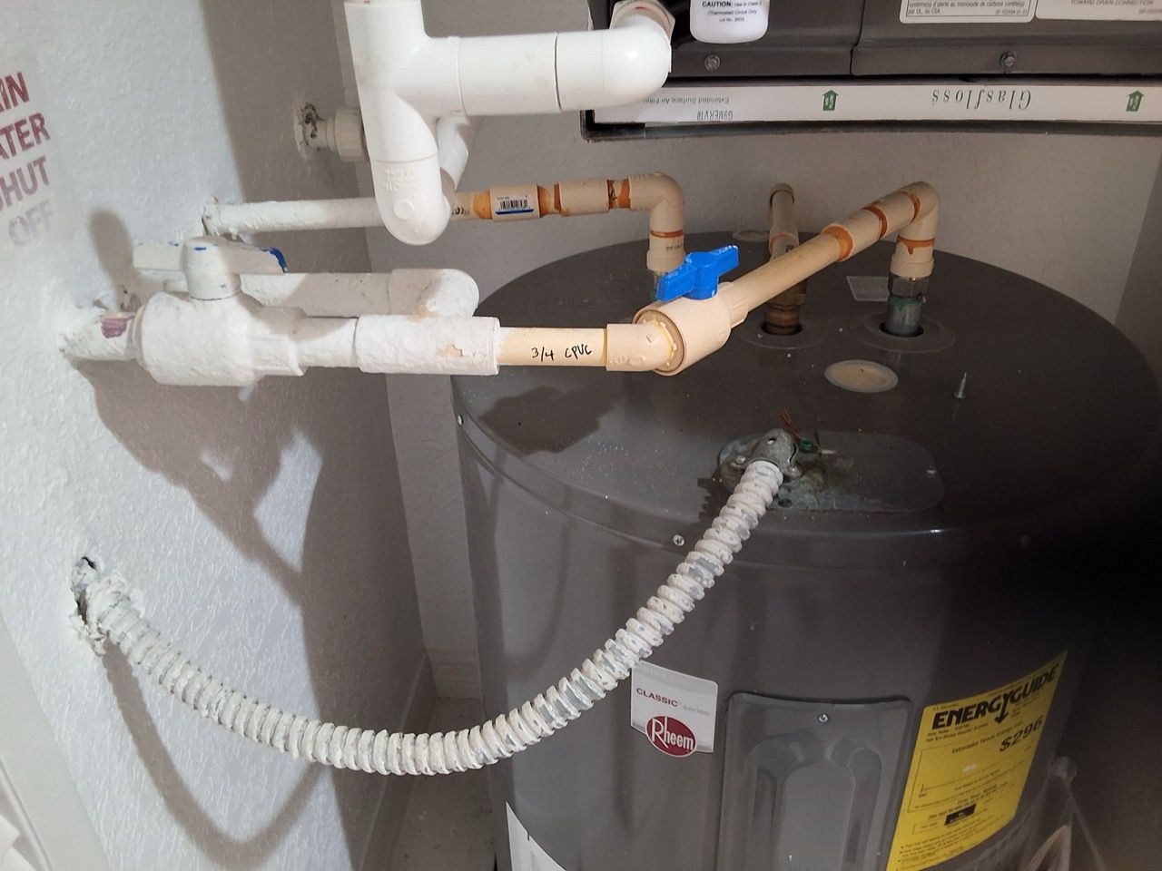 Basement water heater with copper pipes, white PVC plumbing, and a coiled drain hose.