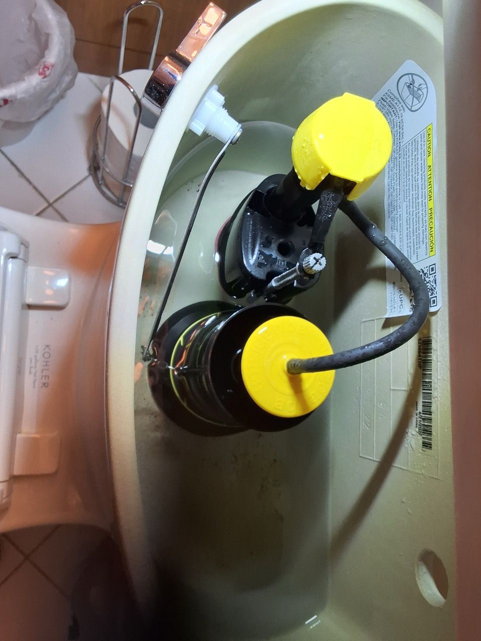 Two black toilet tank parts with yellow caps inside an open toilet tank.