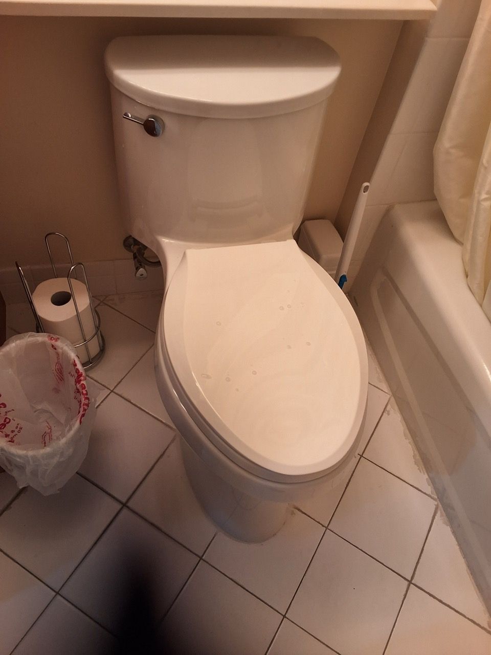 Small bathroom with a white toilet and tiled floor, with a toilet brush and waste bin beside it.
