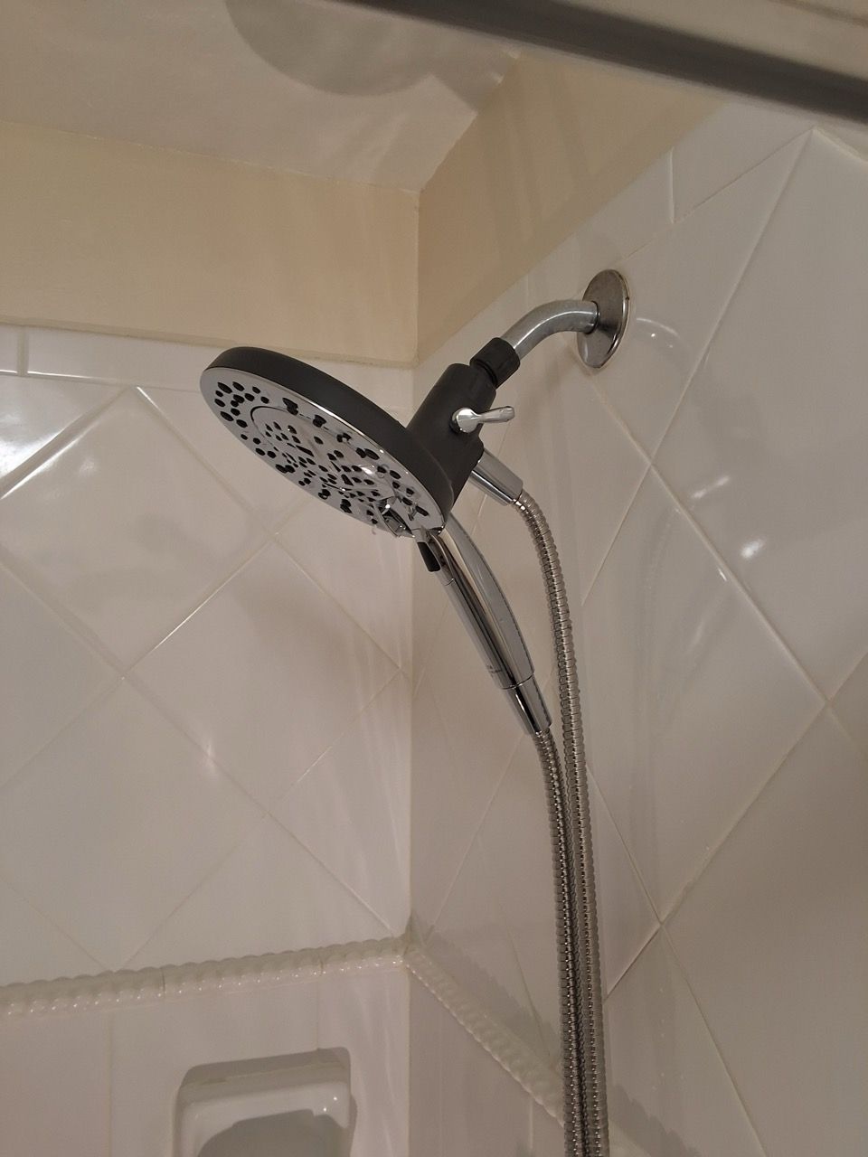 Chrome handheld showerhead mounted on tiled bathroom wall, with flexible hose.
