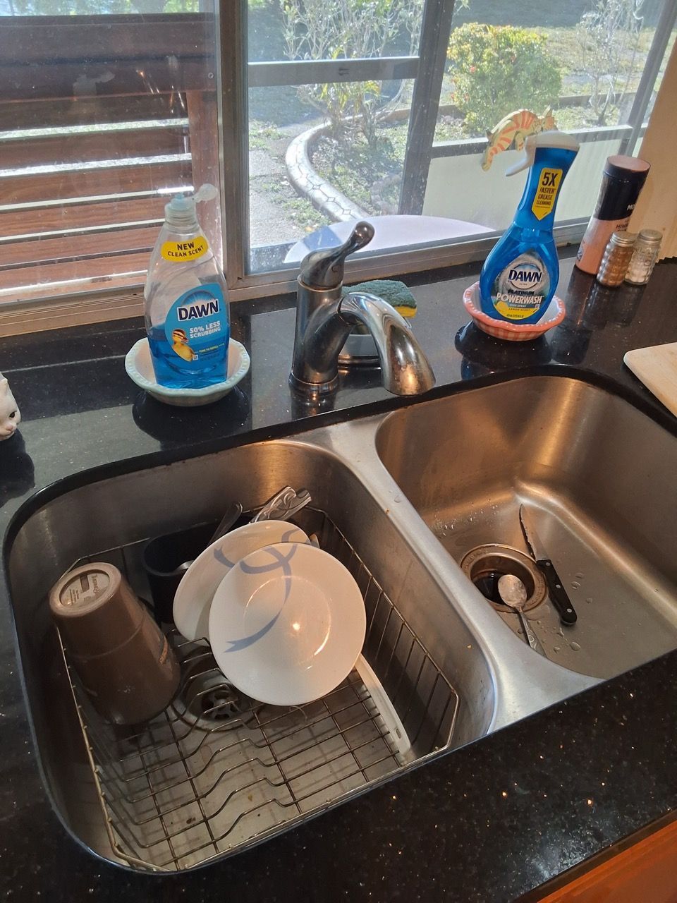 Kitchen sink with stacked dishes and a soap dispenser on the counter, sunlight coming through the window.