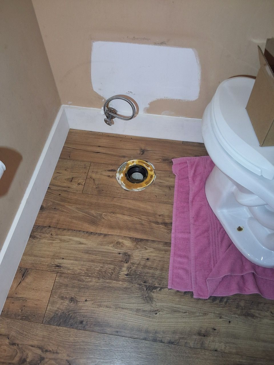 Bathroom floor with toilet, exposed drain, and a pink towel on the floor